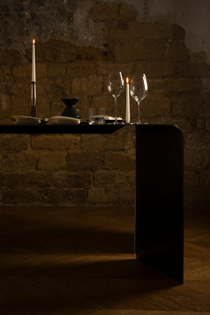 Darkly lit table setting with candles and wine glasses against a stone wall.