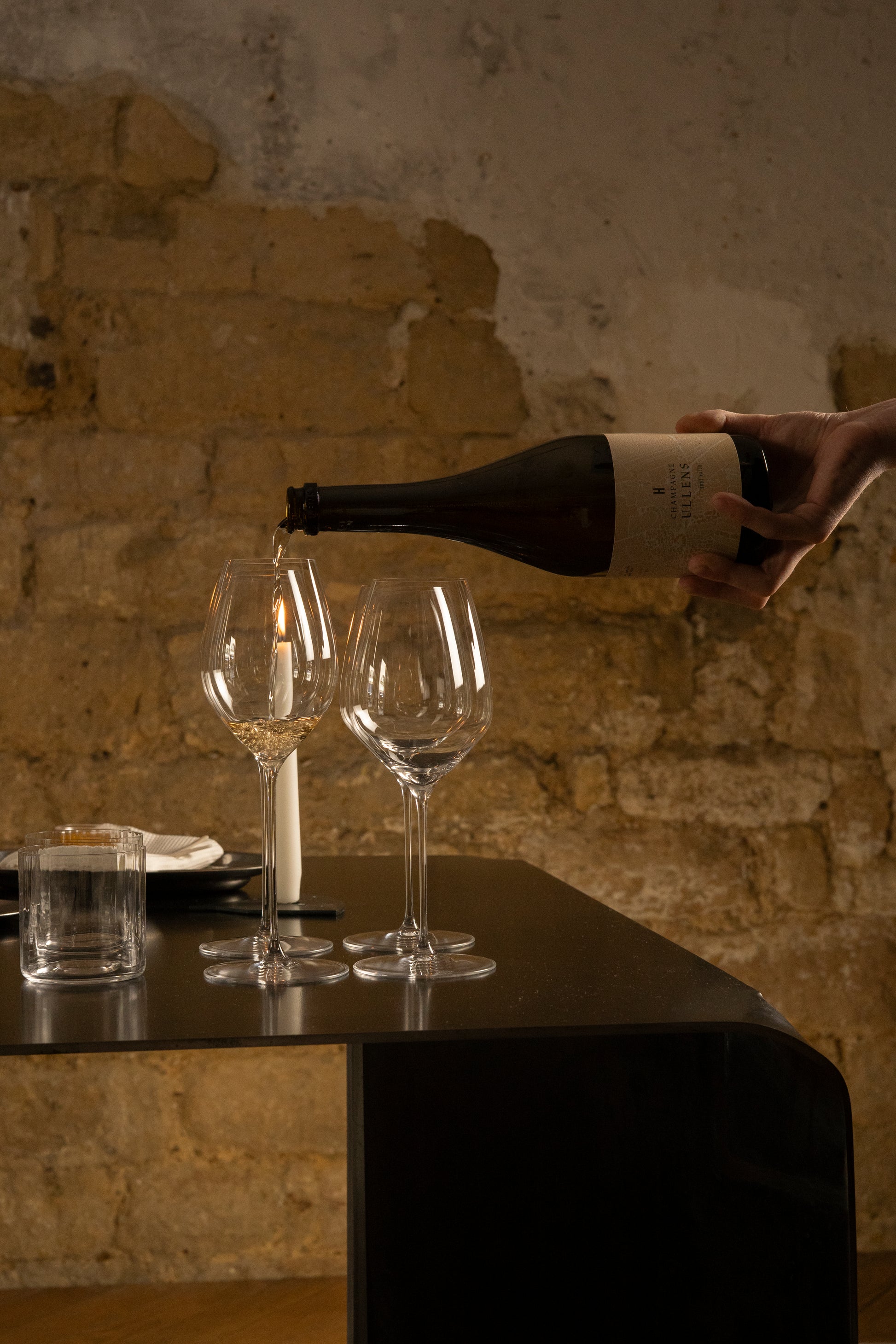 Person pouring wine into two glasses with a bottle in a rustic setting.